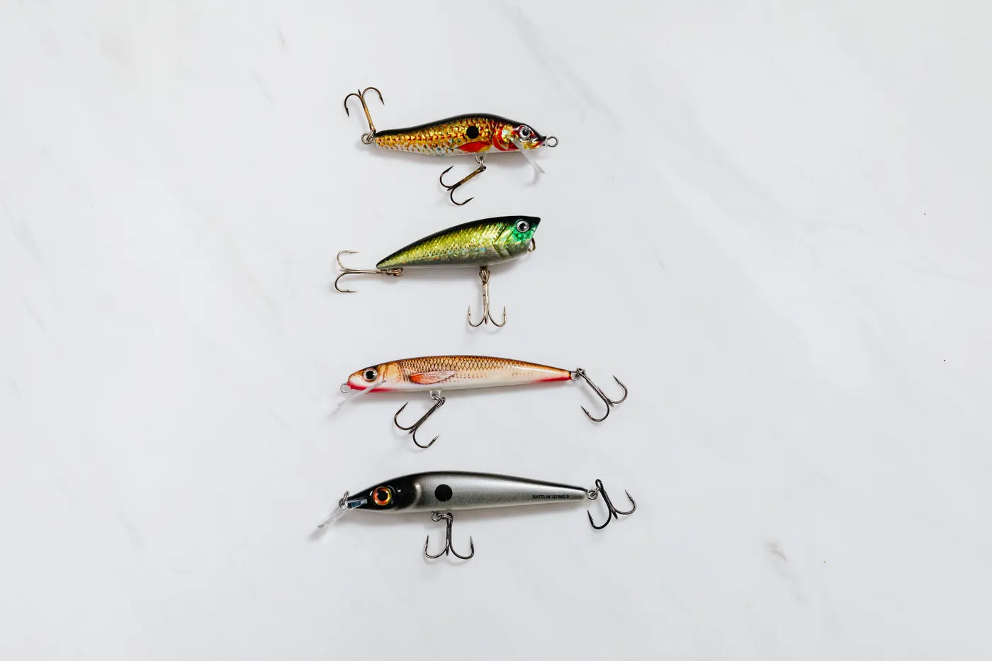 Four fishing lures with hooks laid out on a white surface